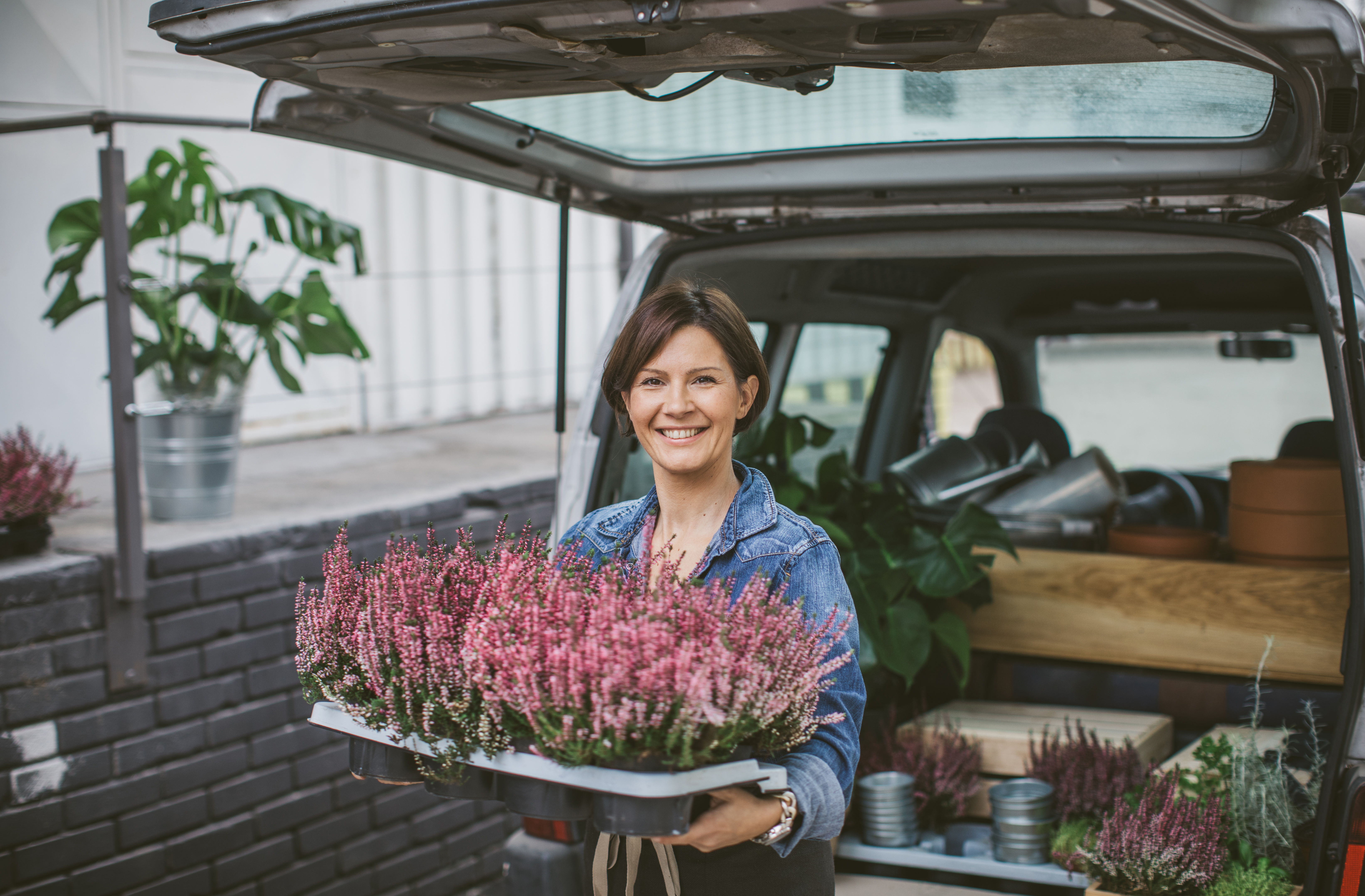 Leende kvinna fyller bagageutrymmet på en bil med blommor av olika sorter