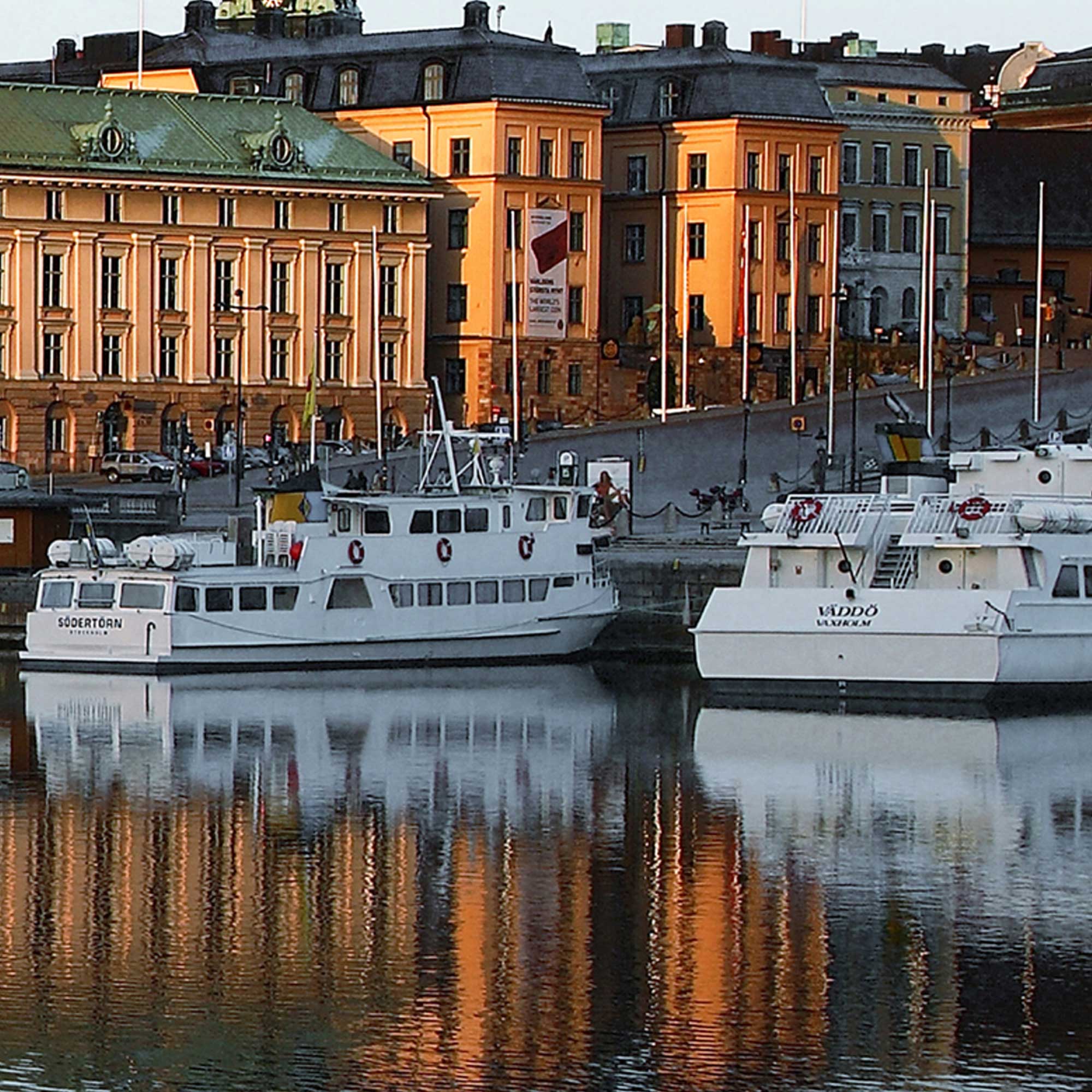 Gamla stan i Stockholm. Vy vid vattnet med två vita båtar, gator och gula byggnader i bakgrunden