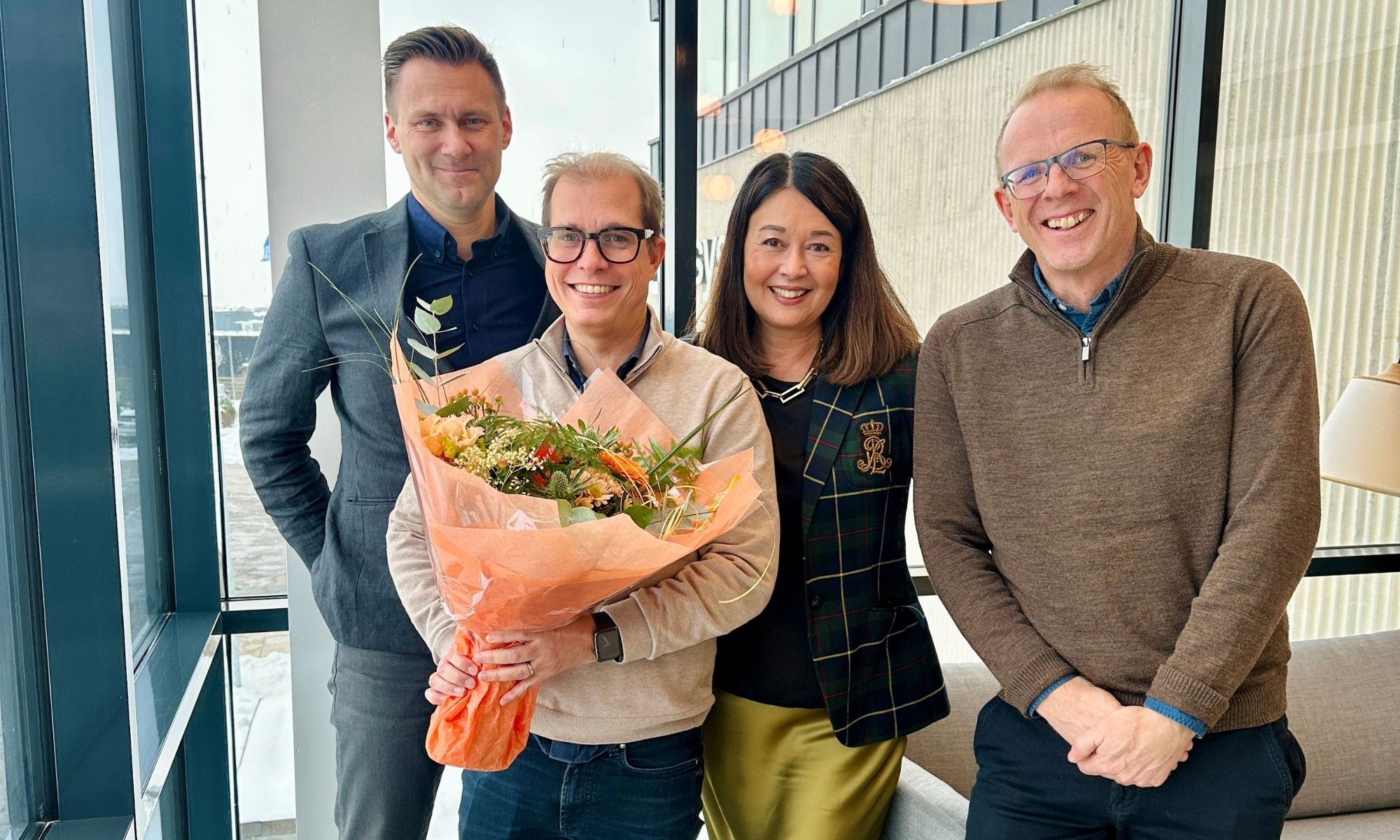 Fyra glada kollegor med en blombukett