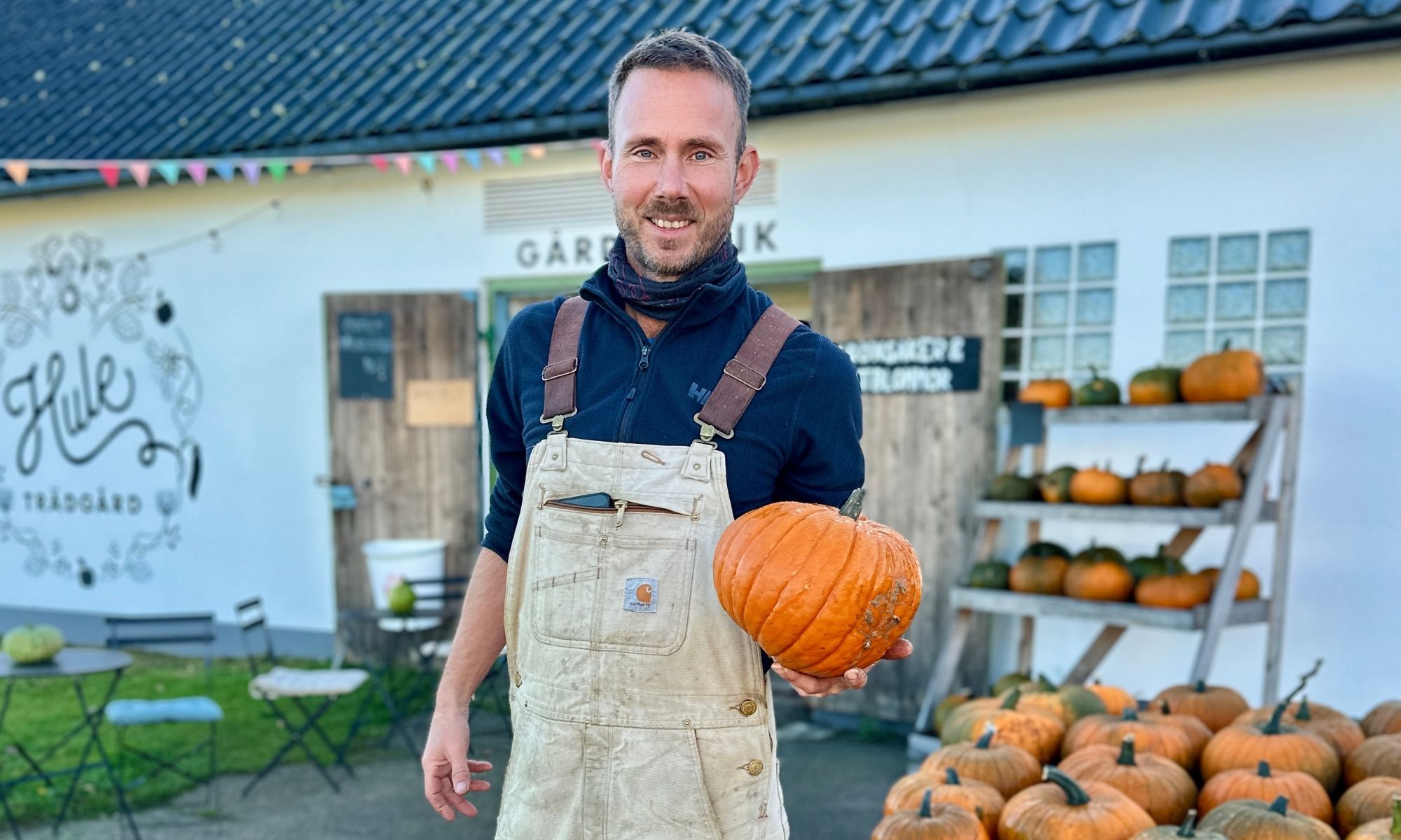 Leende man framför en gårdsbutik som visar upp en pumpa