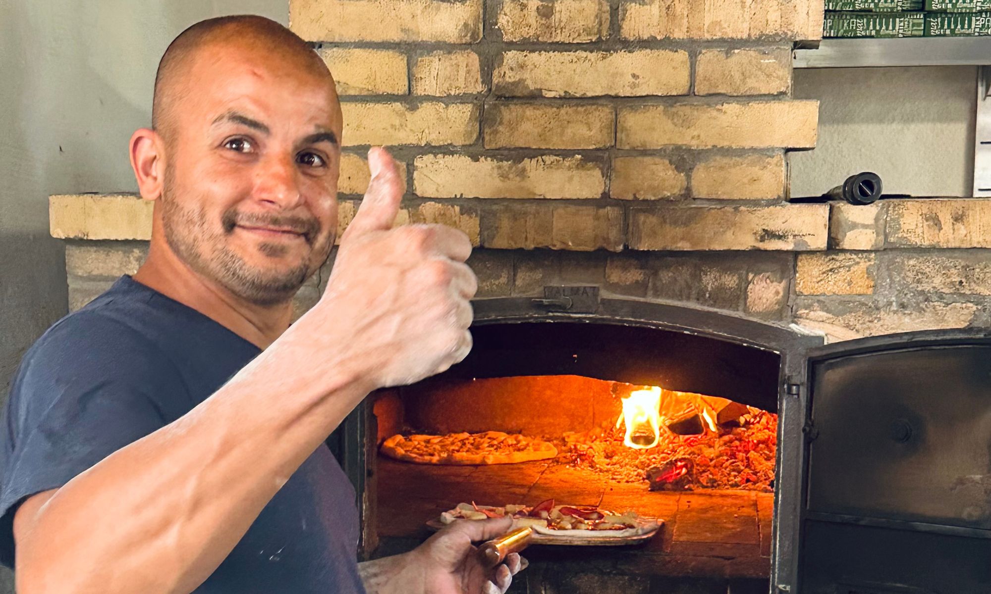 Leende man står framför en pizzaugn påväg att tillaga en pizza