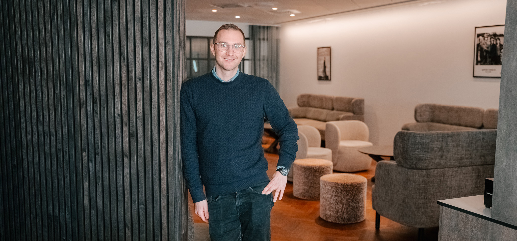 Man i ett kontorslandskap, står med höger axel lutad mot en vägg